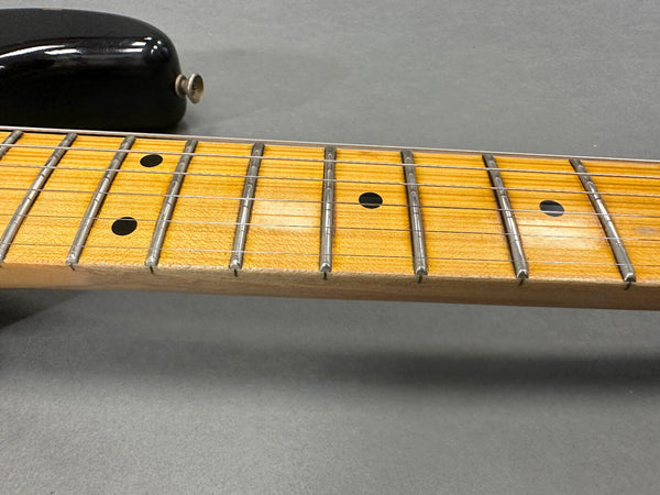 Close-up of maple guitar fretboard with black dot inlays and metal frets on electric guitar neck with black body edge on gray background
