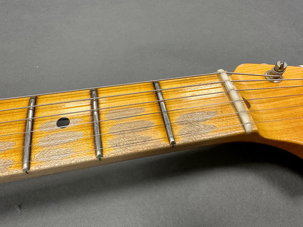 Close-up image of guitar neck showing worn maple fretboard with metal frets, dot inlay, guitar strings, and nut against a gray background