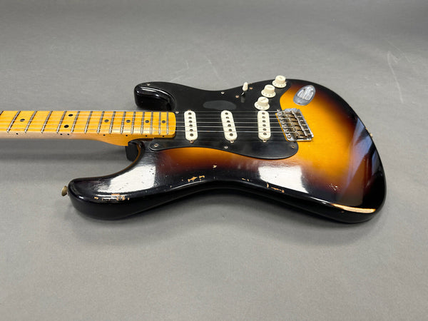 Vintage sunburst electric guitar with maple neck and black pickguard showing worn finish and three single-coil pickups on gray background