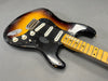 Vintage sunburst electric guitar with worn finish, maple neck, black pickguard, and three single-coil pickups displayed on gray background
