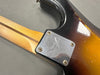 Close-up of Fender electric guitar neck plate with serial number on sunburst body and maple neck with skunk stripe