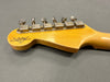 Back of a vintage Fender Custom Shop guitar headstock with six metal tuning pegs on a light wood neck against a gray background