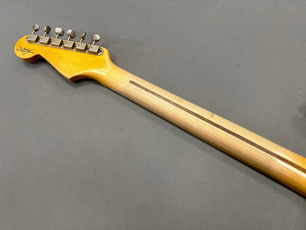 Back view of a Fender electric guitar neck showing tuners and maple wood grain on grey background