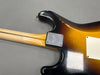 Close-up of the back of a sunburst electric guitar body and neck joint with a metal neck plate and visible wear and scratches on the finish
