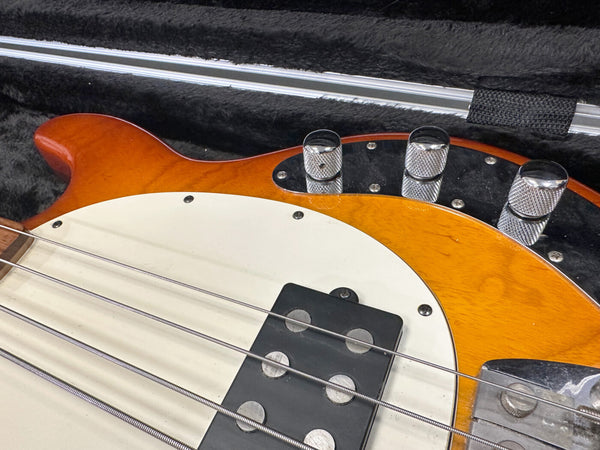 Close-up of electric bass guitar body with sunburst finish, white pickguard, black pickup, and chrome control knobs in black plush case