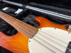 Close-up of orange electric bass guitar with rosewood fretless fingerboard and white pickguard in black plush guitar case