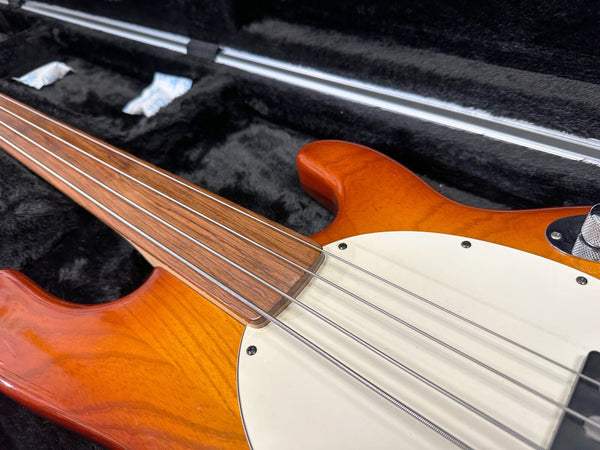 Close-up of orange electric bass guitar with rosewood fretless fingerboard and white pickguard in black plush guitar case