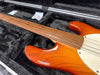 Close-up of fretless electric bass guitar neck and body in orange sunburst finish inside black plush-lined guitar case