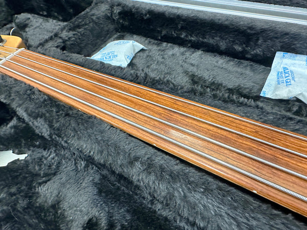 Close-up of rosewood fretless bass guitar neck with metal strings resting in black plush guitar case with silica gel packets