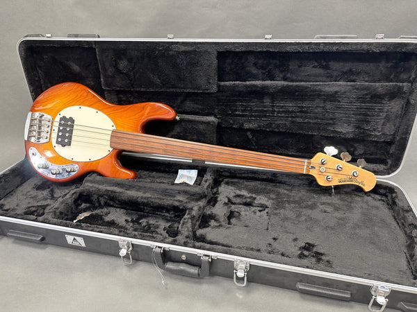 Ernie Ball Music Man StingRay fretless bass guitar with natural wood finish and cream pickguard in a black plush-lined hard case