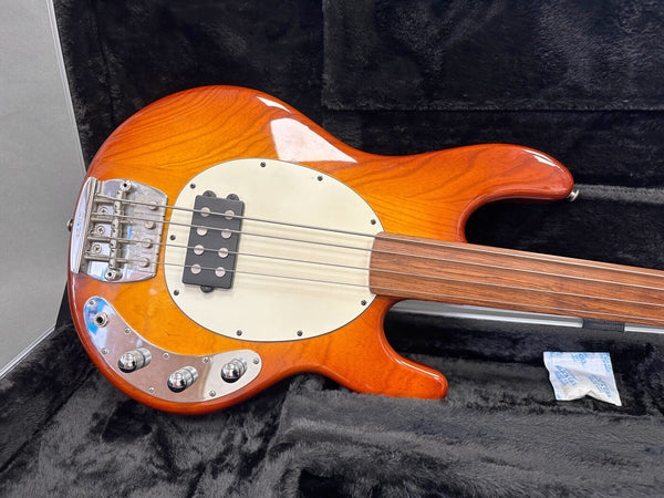 Close-up of archtop electric bass guitar with sunburst finish, single humbucker pickup, chrome control knobs, and rosewood fretless fingerboard in black plush guitar case