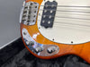 Close-up of orange electric bass guitar body showing chrome bridge, black pickup, white pickguard, and control knobs on black plush case background