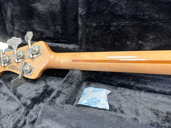 Back of maple guitar neck with tuning pegs and "Made in San Luis Obispo California USA" stamp resting on black plush guitar case interior with silica gel packet