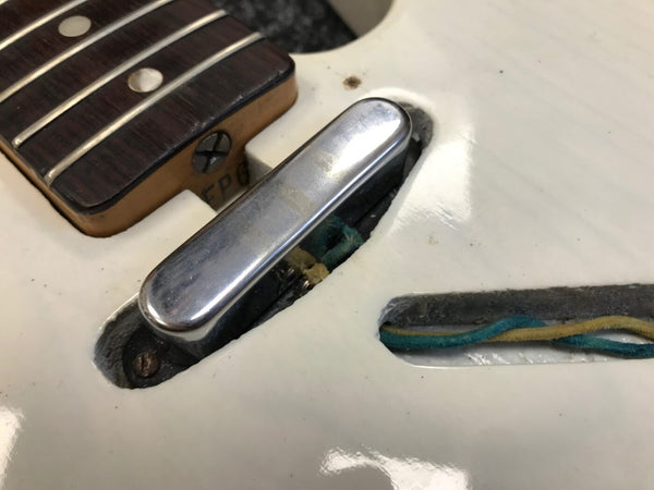Close-up of vintage white electric guitar single coil pickup and pickup cavity showing wiring and part of rosewood fretboard