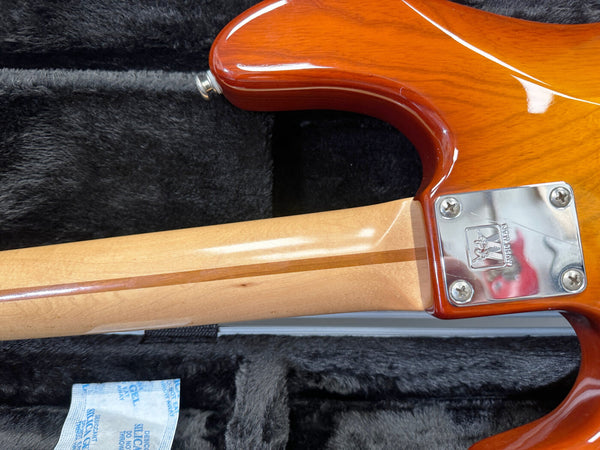 Close-up of guitar neck joint showing maple neck with skunk stripe and chrome neck plate engraved with Washburn logo, inside a black plush guitar case.
