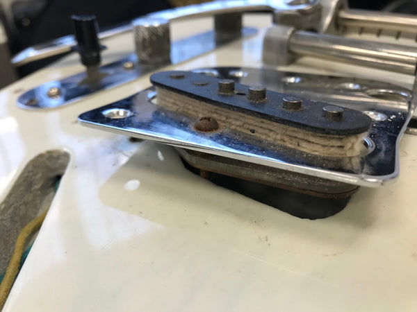 Close-up of vintage electric guitar single-coil pickup with aged wool under the metal cover plate on white guitar body