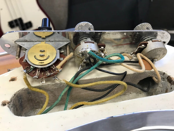 Close-up view of vintage electric guitar control panel wiring and potentiometers inside the guitar body cavity.