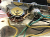 Close-up of vintage guitar control cavity wiring showing potentiometers and cloth-covered wires in cream, green, and black colors inside a cream guitar body cavity.