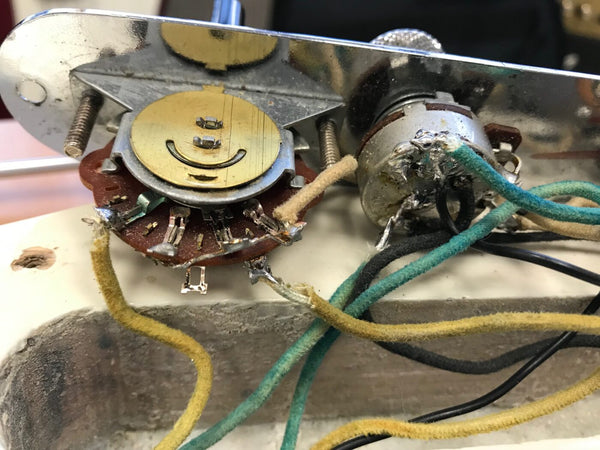 Close-up of vintage guitar control cavity wiring showing potentiometers and cloth-covered wires in cream, green, and black colors inside a cream guitar body cavity.