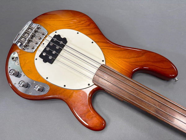 Electric bass guitar with sunburst finish, white pickguard, four metal strings, and chrome control knobs on gray background.