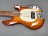 Sunburst electric bass guitar body with white pickguard, chrome hardware, and four strings on gray background