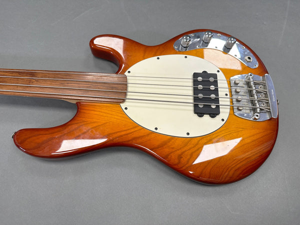 Sunburst electric bass guitar body with white pickguard, chrome hardware, and four strings on gray background
