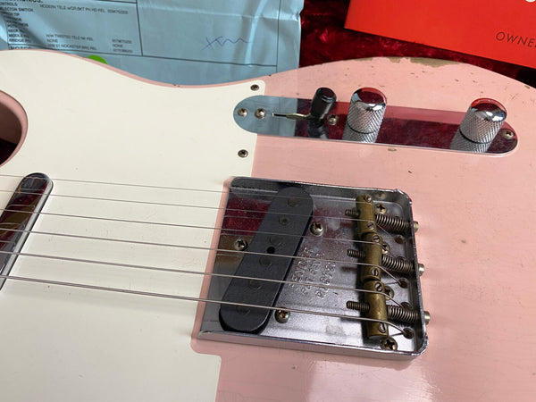 Close-up of pink and white vintage Fender Telecaster electric guitar body showing wear, metal bridge with springs and single-coil pickup, chrome control plate with two control knobs and selector switch, and guitar strings.