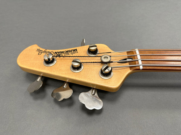 Ernie Ball Music Man StingRay bass guitar headstock with tuning pegs and strings close-up on gray background