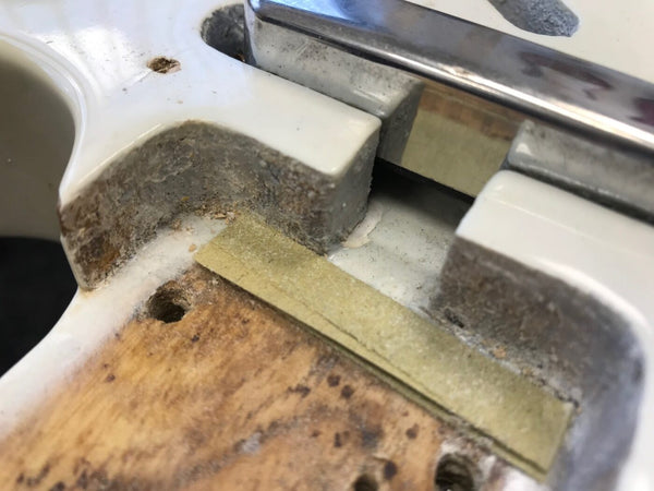 Close-up of electric guitar body cavity showing worn white paint, wood grain, and shielding tape for electronics, highlighting internal guitar construction details.