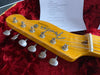 Close-up of Fender Telecaster guitar headstock with tuning pegs, strings, and logo on yellow wood finish, resting inside red plush guitar case