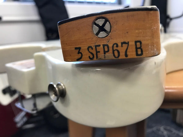 Close-up of guitar neck heel stamped with serial number 3 SFP67 B, attached to white guitar body with metal strap button.