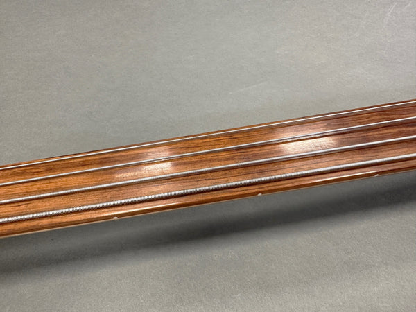 Close-up of guitar fretless fingerboard with metal strings on wooden neck against gray background