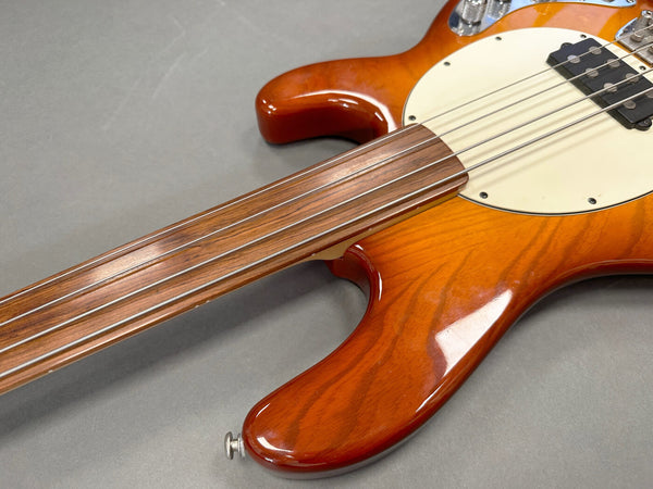 Close-up of fretless electric bass guitar neck and body with sunburst finish and white pickguard on gray background