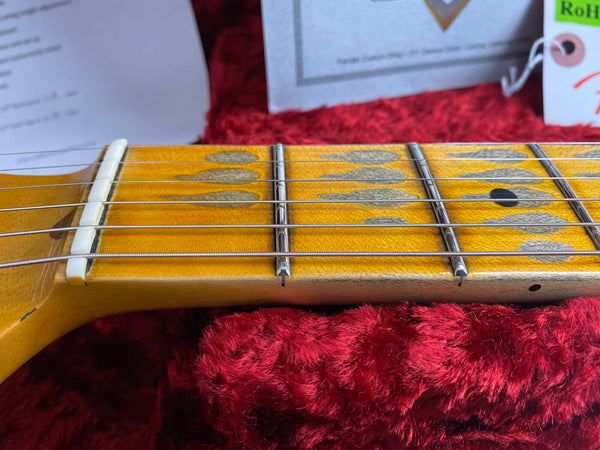 Close-up of a vintage guitar maple neck and fretboard with unique teardrop inlays, steel guitar strings, and detailed frets resting on red plush guitar case lining.