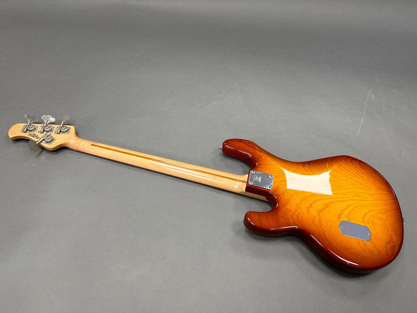 Back view of sunburst electric bass guitar with maple neck and chrome tuning pegs on gray background