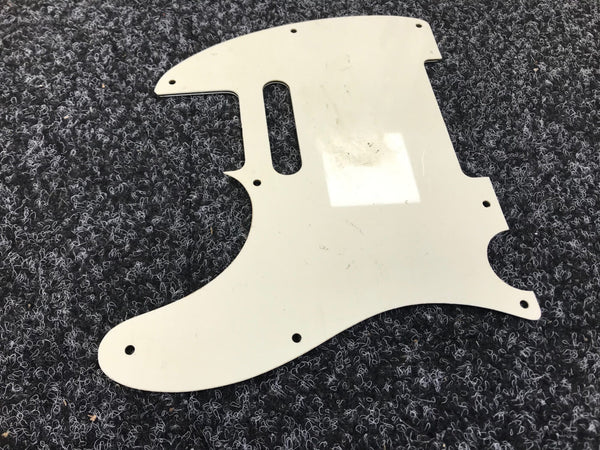 White guitar pickguard for Fender Telecaster with scratches and mounting holes on dark textured carpet background