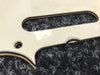 Close-up of white guitar pickguard with screw hole and black textured background showing wear and discoloration details