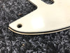 Close-up of white guitar pickguard corner with black and cream layered edging on textured black and white fabric background
