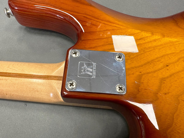Close-up of guitar neck joint with metal neck plate engraved with Music Man logo on sunburst finish electric guitar body