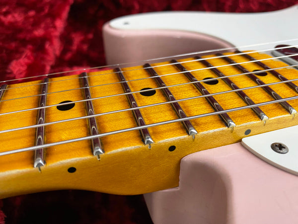 Close-up of maple guitar neck and fretboard with dot inlays on pink solid body electric guitar against red velvet background