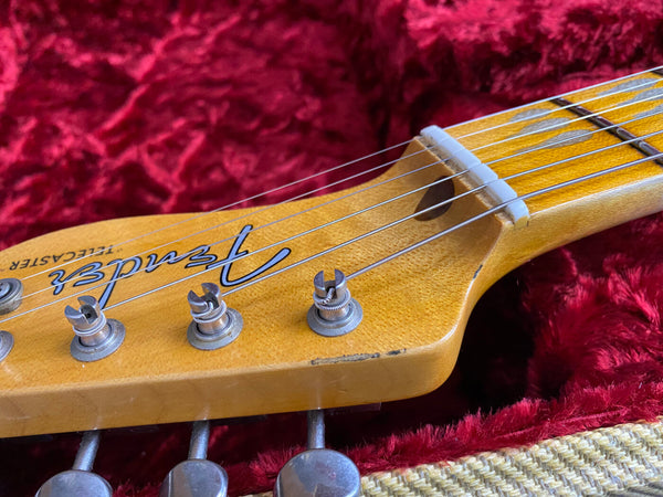 Close-up of Fender Telecaster guitar headstock with tuning pegs and strings on red plush guitar case interior