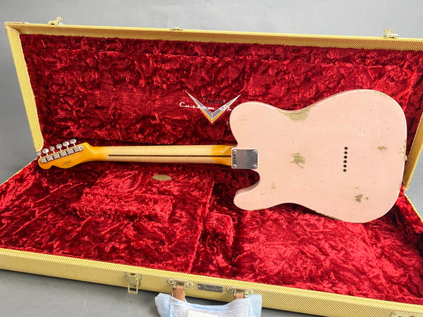 Back of pink Fender Telecaster electric guitar with visible wear, resting in open Fender Custom Shop tweed guitar case with red plush interior lining
