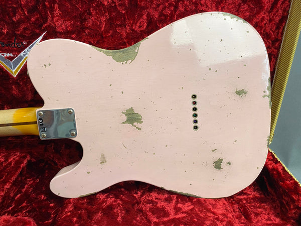 Back of vintage pink electric guitar with visible paint wear and six string ferrules, resting on red plush interior of Fender guitar case
