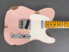 Close-up of worn pink electric guitar body with white pickguard and maple fretboard on gray background