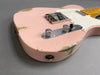 Close-up of worn pink electric guitar body with chrome control knobs and white pickguard on gray background