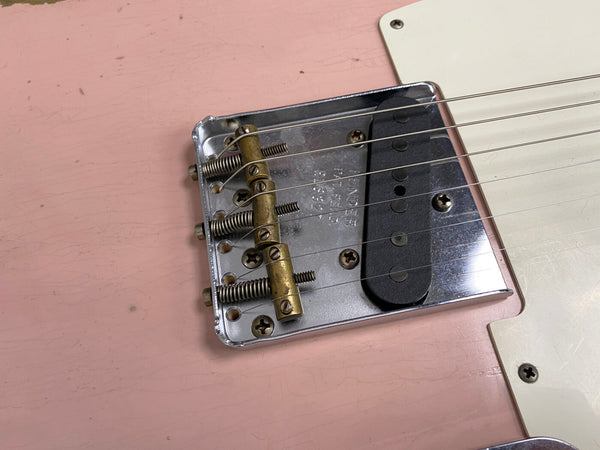 Close-up of vintage Fender Telecaster guitar bridge with brass saddles and single-coil pickup on pink body