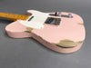 Vintage pink electric guitar with worn and chipped paint showing wood grain, featuring a white pickguard, chrome bridge, and maple fretboard on gray background