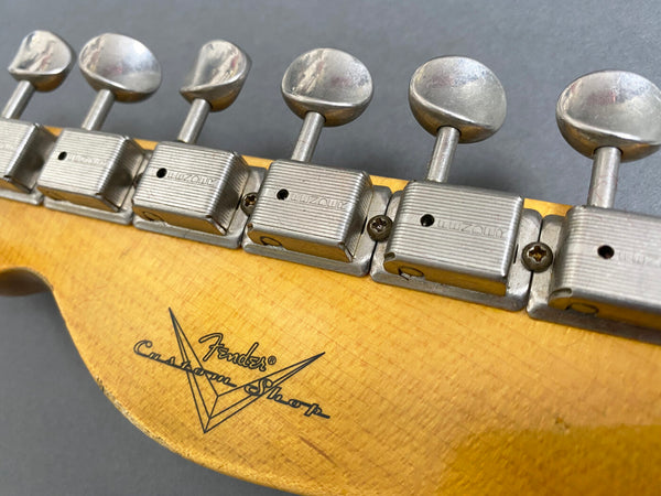 Close-up of vintage Fender Custom Shop guitar headstock with metal tuning pegs and logo on worn wood finish