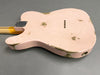 Back of vintage distressed pink electric guitar body with worn paint and string ferrules on a gray background