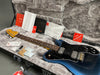 Fender electric guitar in metallic blue finish with rosewood fretboard, black pickguard, and chrome hardware, displayed inside a plush gray hardshell case with Fender manuals, setup instructions, warranty card, and accessories.